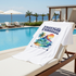 White T-Shirt with 'Tropical Paradise' design on a lounge chair by a pool with ocean view