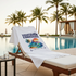White t-shirt with 'Tropical Paradise' design on a lounge chair by a pool with palm trees in the background.