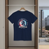 Navy blue t-shirt with 'Independence Day America 4th July' design on a hanger in a room with a cityscape view.