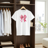 White t-shirt with pink bow design hanging in a wardrobe.