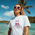 Woman wearing white cotton-blend T-shirt with pink cherry graphic and bow at the beach, pink sunglasses