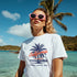 Woman wearing white California graphic T-shirt with palm design on a sunny beach (sizes S–XL).