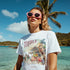 Woman wearing white Tequila graphic T-shirt on a tropical beach with pink sunglasses.