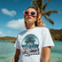 White Tropical Beach graphic tee with palm tree design and Summer Beach text worn by a woman at the sunny shore
