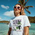 Grapes Graphic T‑Shirt for women in white cotton blend with grape print, short sleeves; model at the beach.