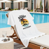 Towel with 'Tropical Sunset Beach Resort' design on a lounge chair by a pool.