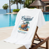 White t-shirt with a coconut graphic and text on a lounge chair by a poolside.