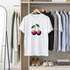 White t-shirt with cherry design hanging in a wardrobe with other clothes.