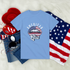 Blue t-shirt with 'American Girl' design, sunglasses, denim jeans, and American flag on a white background