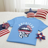 Blue t-shirt with 'American Girl' design on a bed with decorative items.