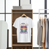 White t-shirt with colorful graphic design hanging on a wooden rack in a clothing store.