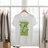 White t-shirt with a green graphic design on a hanger in a clothing store.