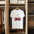 White t-shirt with cherry design hanging in a wardrobe with clothes and shoes.