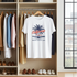 White t-shirt with 'California' design hanging in a wardrobe with clothes and shoes below.