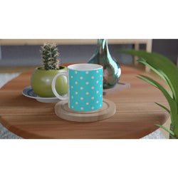 Aqua blue ceramic mug with white polka dots sits on a wooden coaster, featuring a cute retro design next to a small cactus.