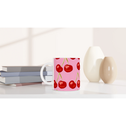 Pink cherry-print mug with white handle on a desk, a cute coquette aesthetic coffee cup.