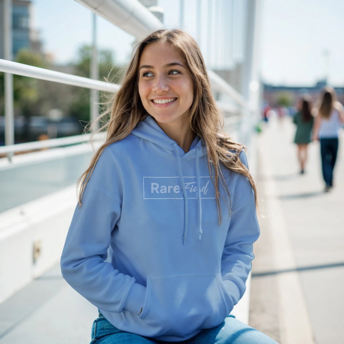 Woman in a light blue Rare Find hoodie with front pocket, outdoors near an urban railing, smiling.