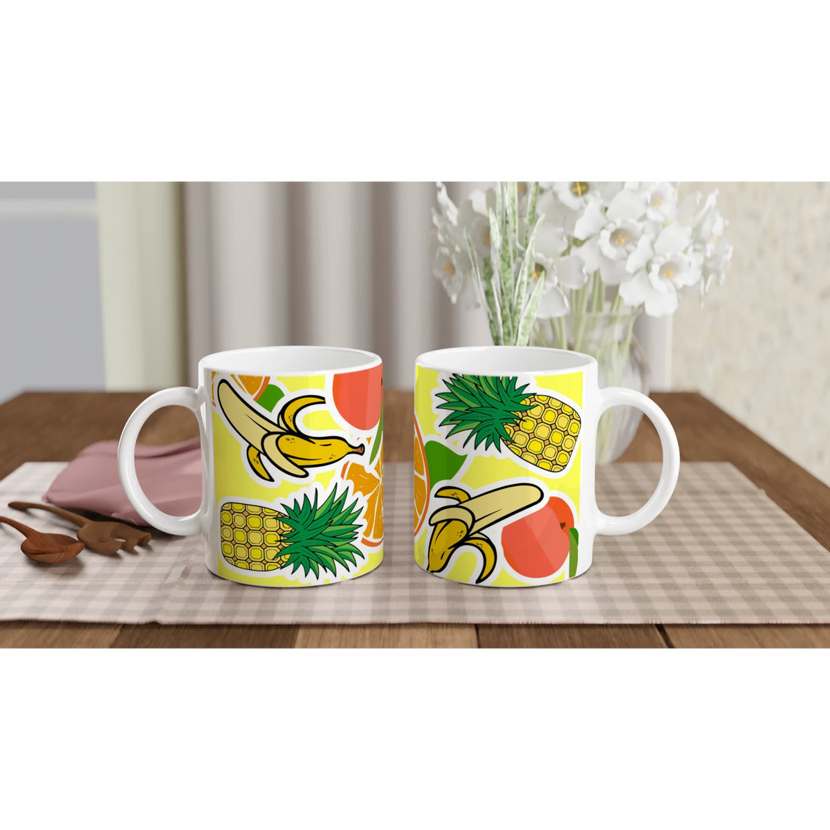 Two white ceramic mugs featuring a vibrant tropical fruit design with bananas, pineapples, and orange slices on a yellow background.