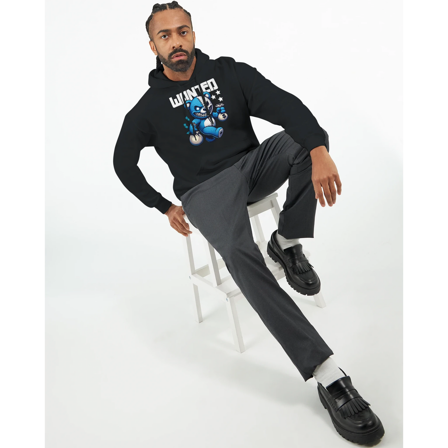 Man sitting on a stool wearing a black men's teddy bear hoodie with graphic design and grey pants.