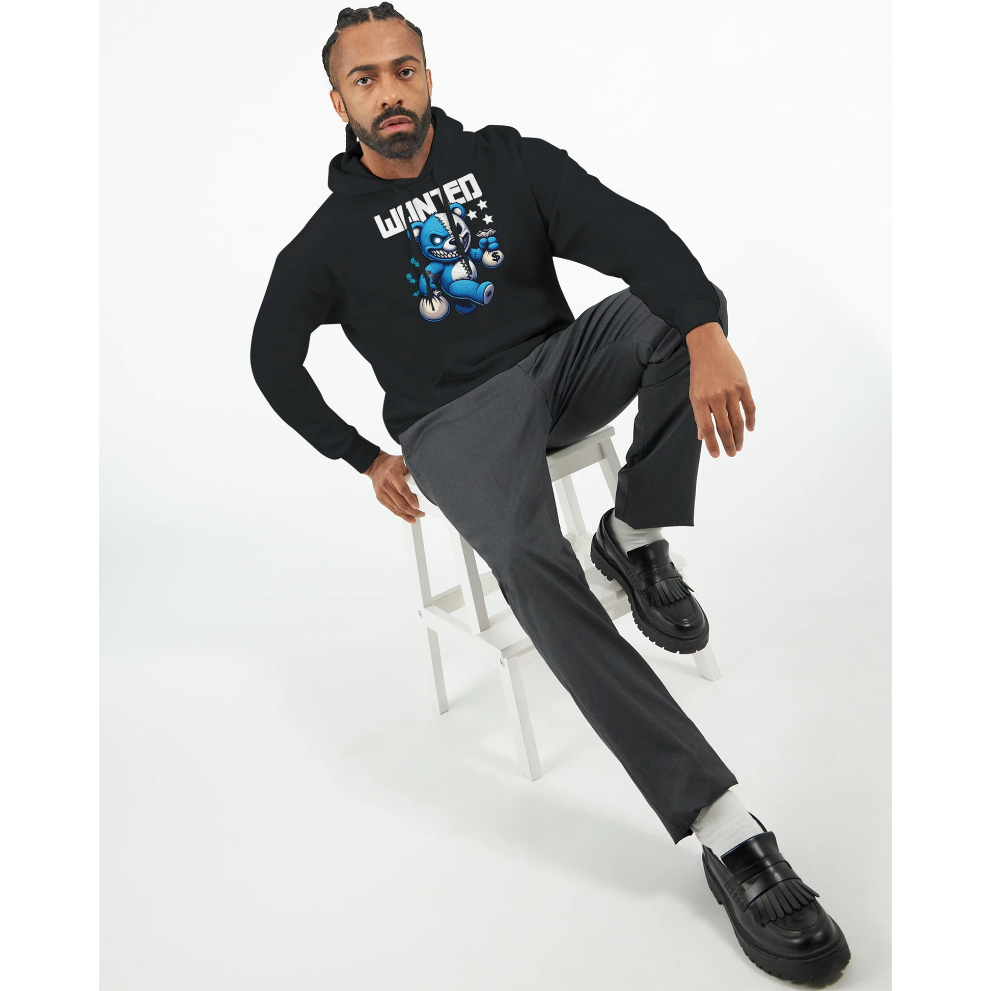 Man sitting on a stool wearing a black men's teddy bear hoodie with graphic design and grey pants.