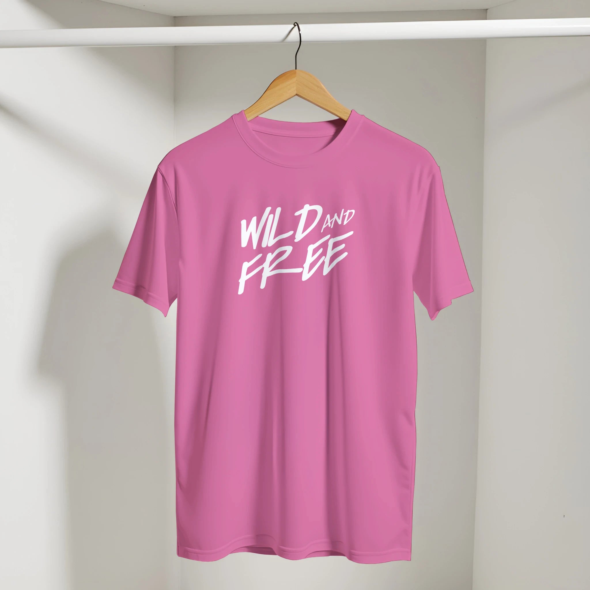 Pink T-shirt on wooden hanger with bold white WILD AND FREE slogan.