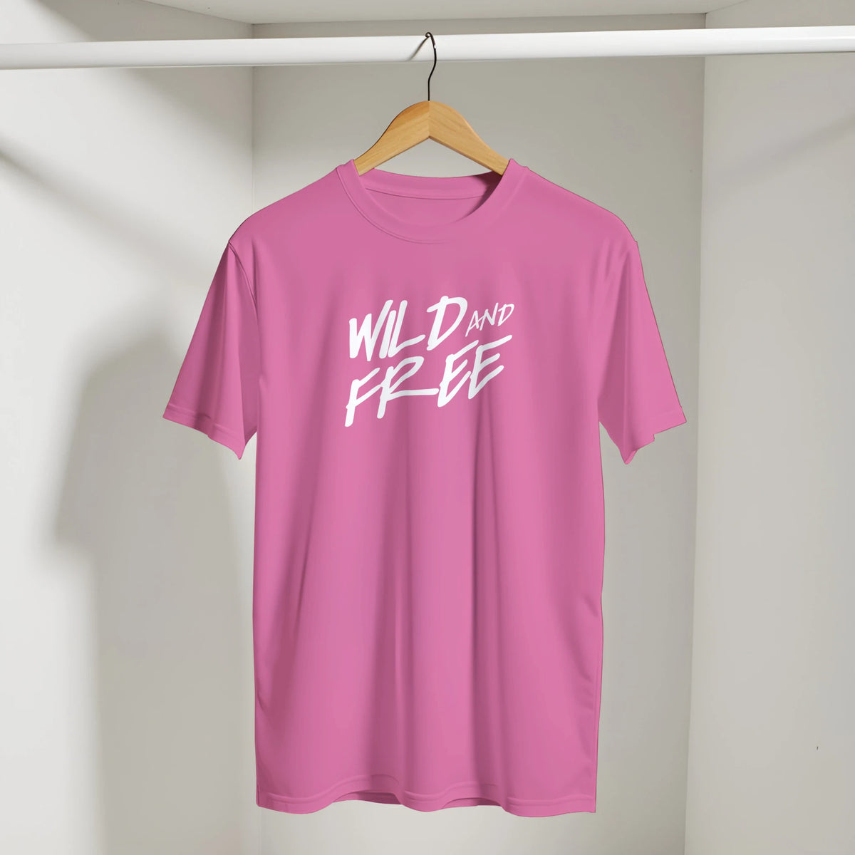 Pink T-shirt on wooden hanger with bold white WILD AND FREE slogan.