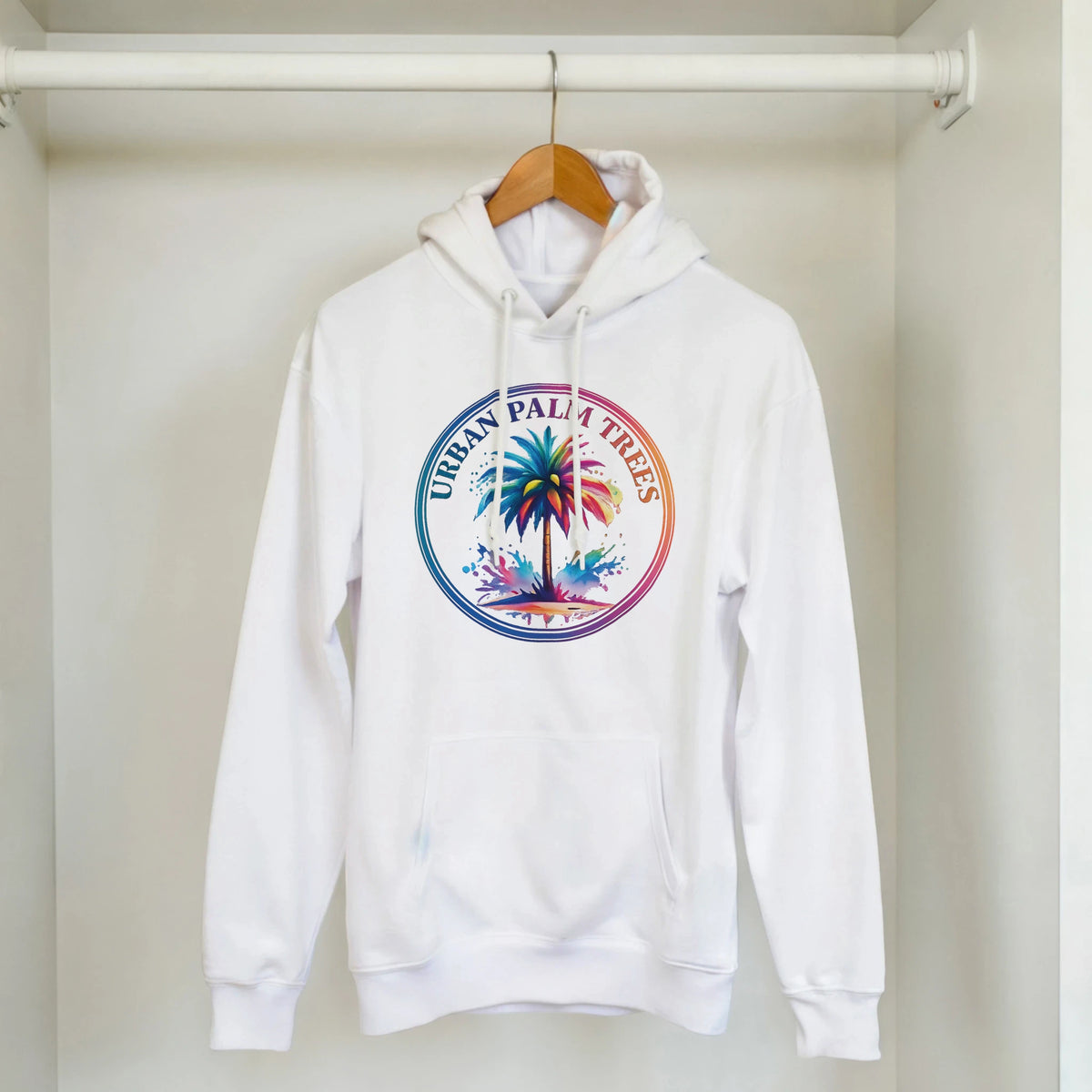 White hoodie on a wooden hanger with a colorful palm-tree circular logo, hanging in a closet.
