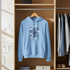 Blue hoodie with text design on a hanger in a wardrobe.
