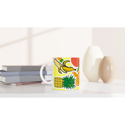 Tropical fruit ceramic mug featuring banana, pineapple and orange design on a white desk with books.