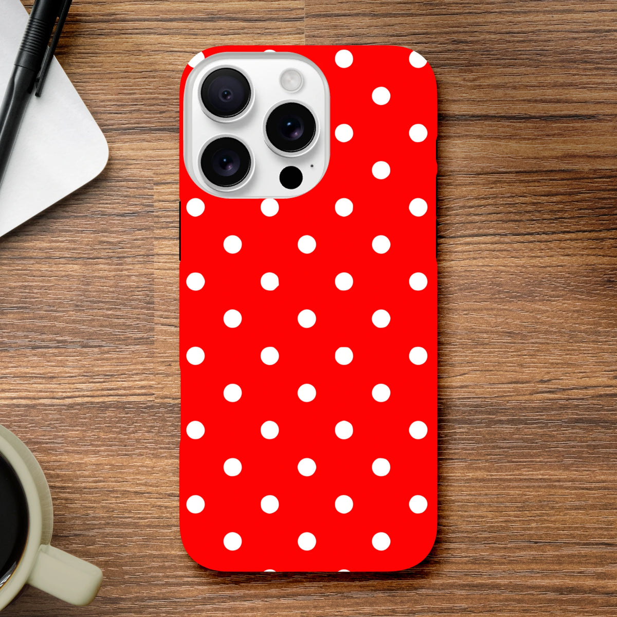 Red and white polka dot tough iPhone case for models 13-16. Cute vintage glossy cover with protective dual-layer TPU shell on wooden desk.