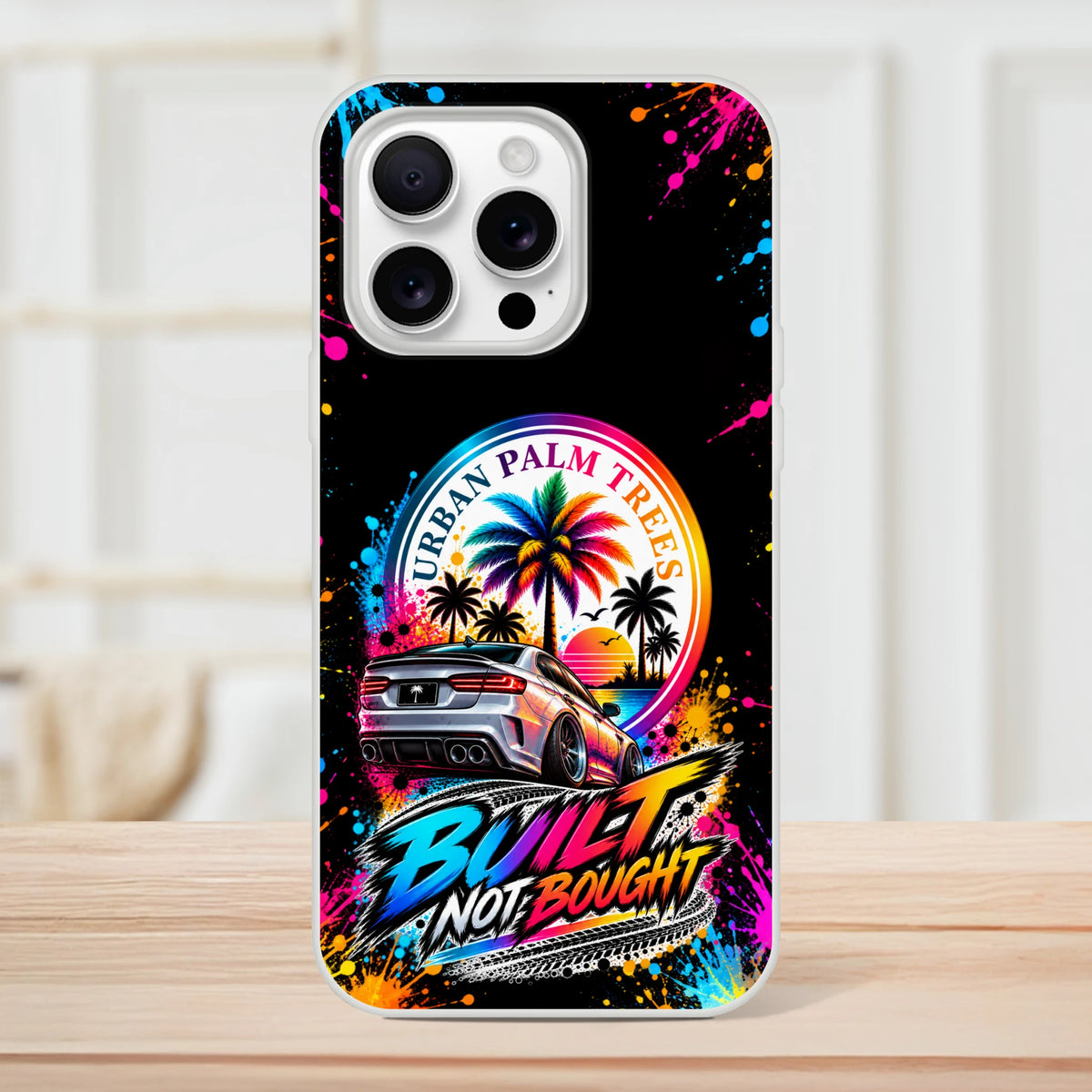 iPhone case featuring a silver drift car, neon "Built Not Bought" text, and colorful Urban Palm Trees sunset graphic with paint splatters.