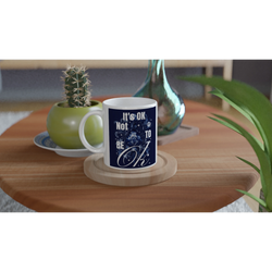 White ceramic mug with navy 'It's OK Not To Be OK' slogan on a wooden coaster, a thoughtful mental health gift.