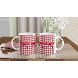 Pair of red gingham bow mugs with red ribbons on a checkered tablecloth.