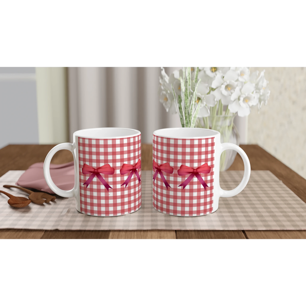 Pair of red gingham bow mugs with red ribbons on a checkered tablecloth.
