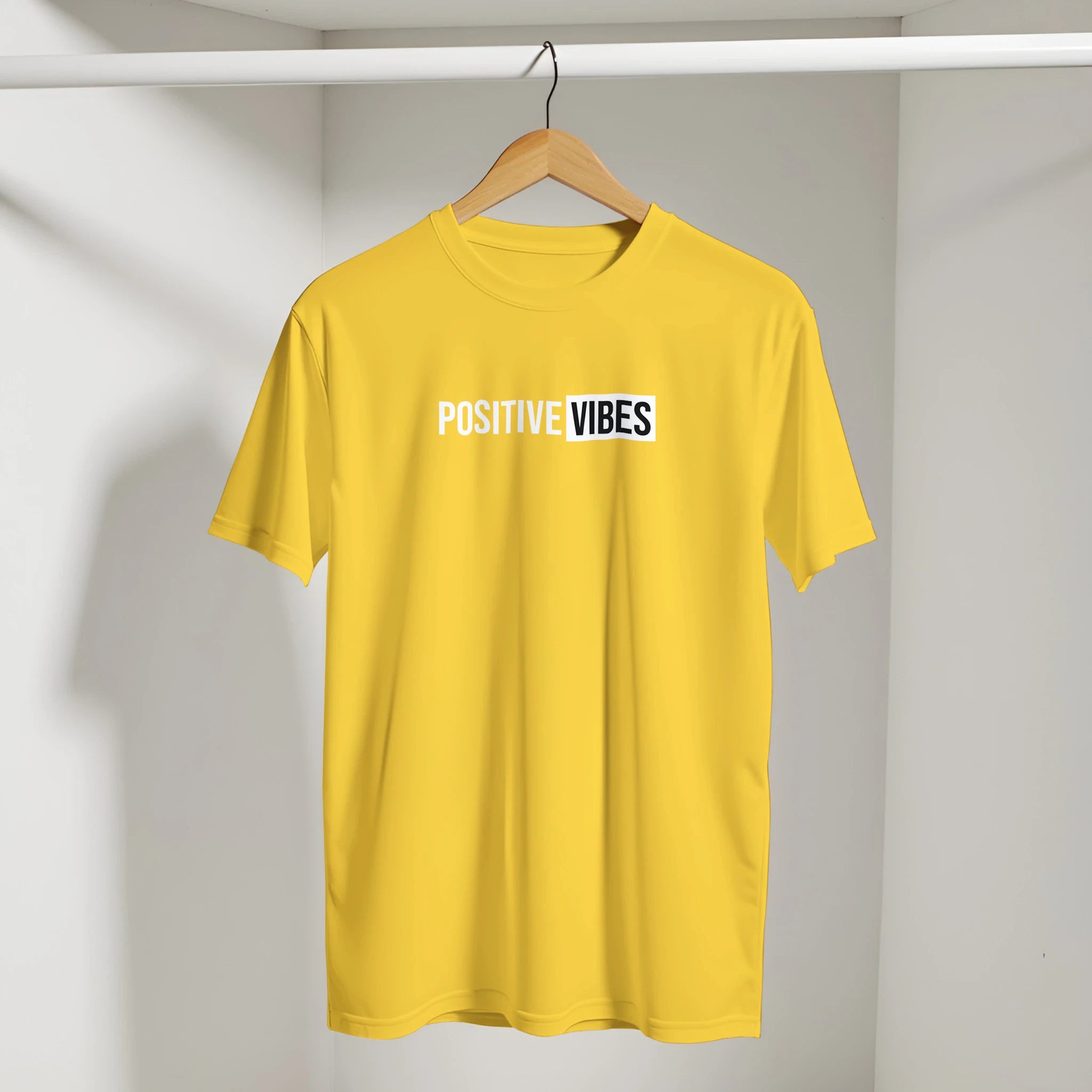 Yellow Positive Vibes T-shirt on a wooden hanger in a closet, retro slogan streetwear look.