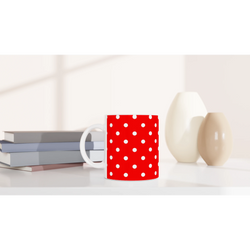 Red and white polka dot ceramic mug sitting on a white desk next to stacked books and decorative vases.