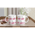 Two white ceramic Glitter Ball Cherries mugs on a checkered placemat with a vase of white flowers in the background.