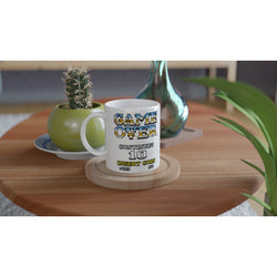 11 oz glossy white mug with pixel GAME OVER design and INSERT COIN on wooden table.