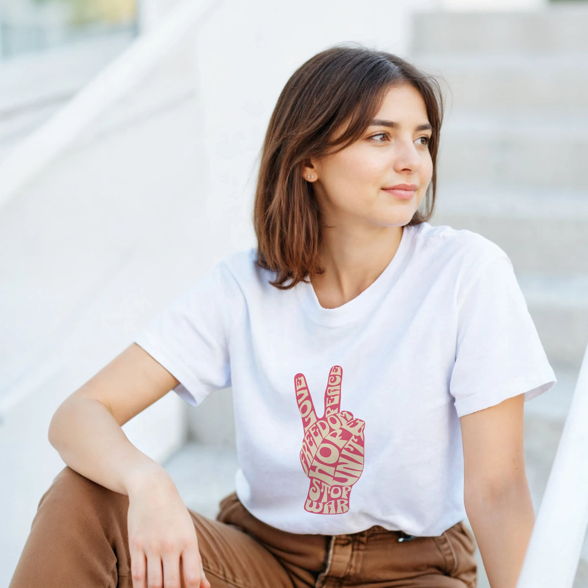 Woman wearing white t-shirt with retro pink typography peace sign graphic featuring words like love, freedom, and stop war.