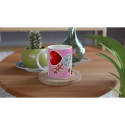 Pink ceramic mug featuring a red heart, disco ball cherry, and bows on a wooden table next to a cactus.