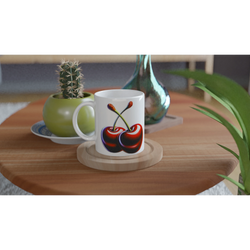 White mug with retro cherry design on a wooden table beside a small cactus and green vase.