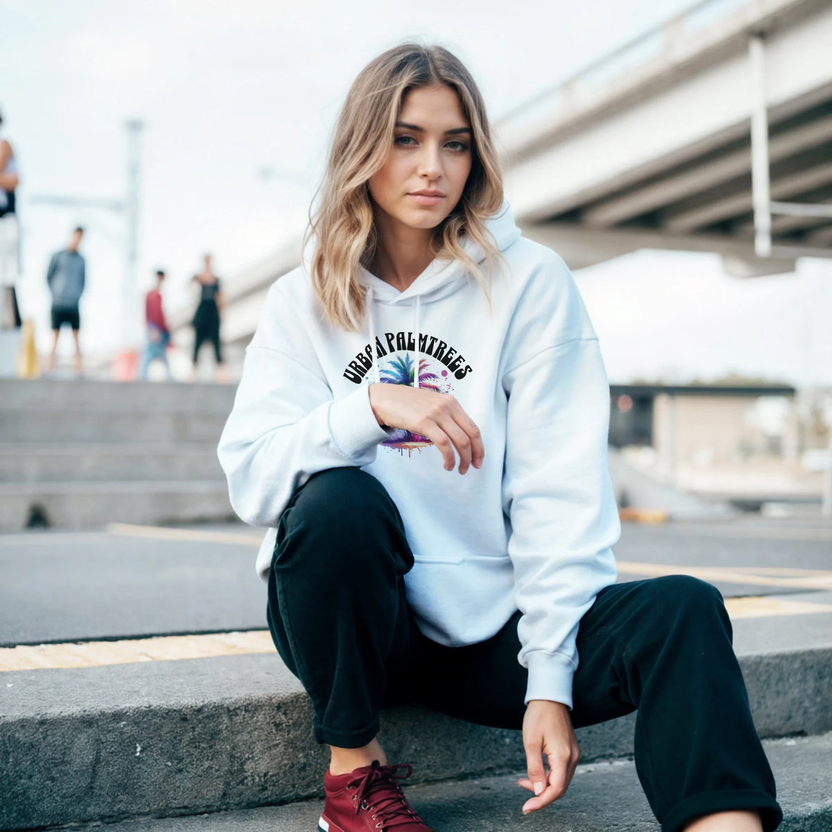 Woman wearing Urban Palm Trees Hoodie, light-blue hoodie with palm trees graphic, sitting on urban steps.