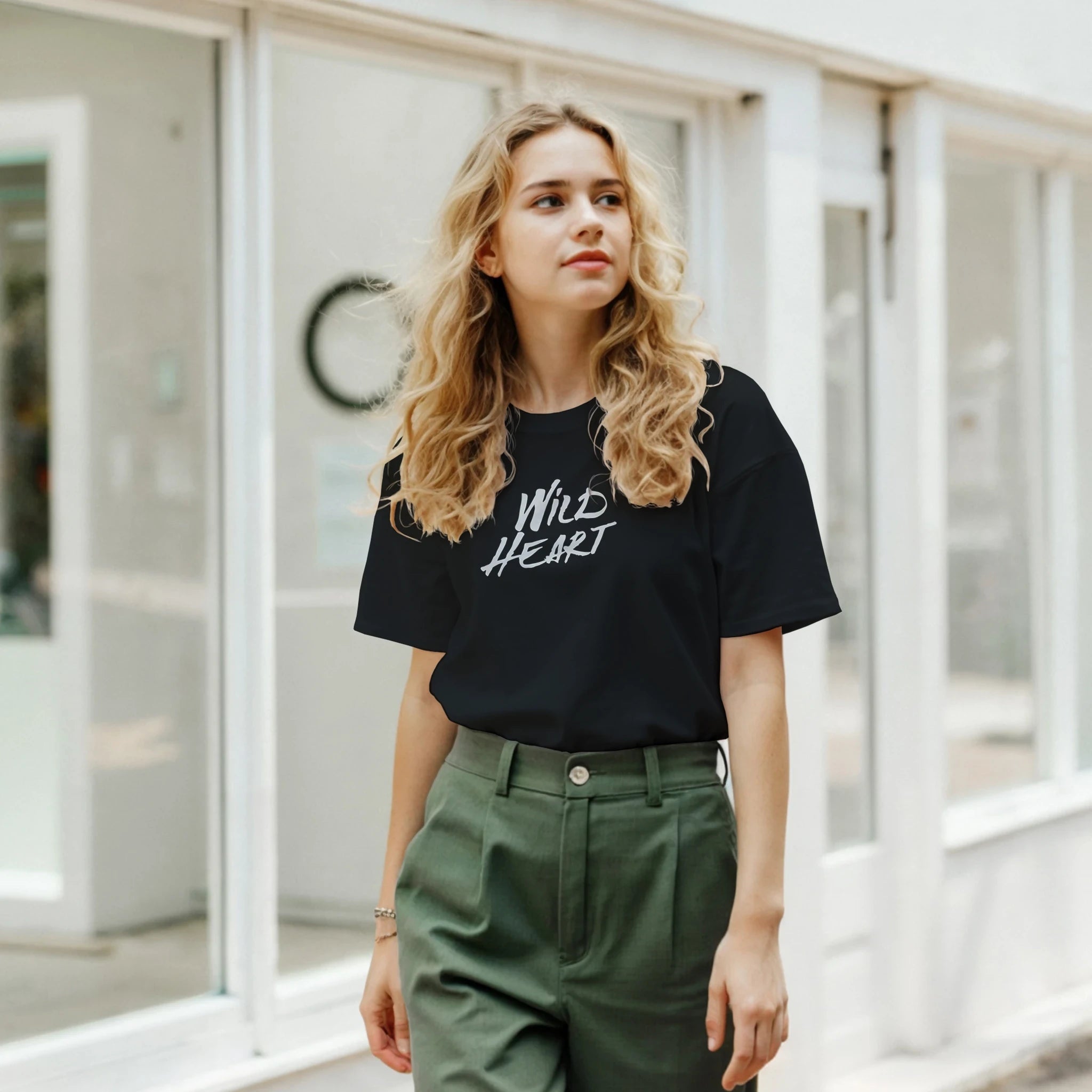 Woman wearing Cute Wild Heart T‑Shirt with retro slogan in an urban street setting, olive-green pants.