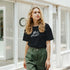 Woman wearing Cute Wild Heart T‑Shirt with retro slogan in an urban street setting, olive-green pants.