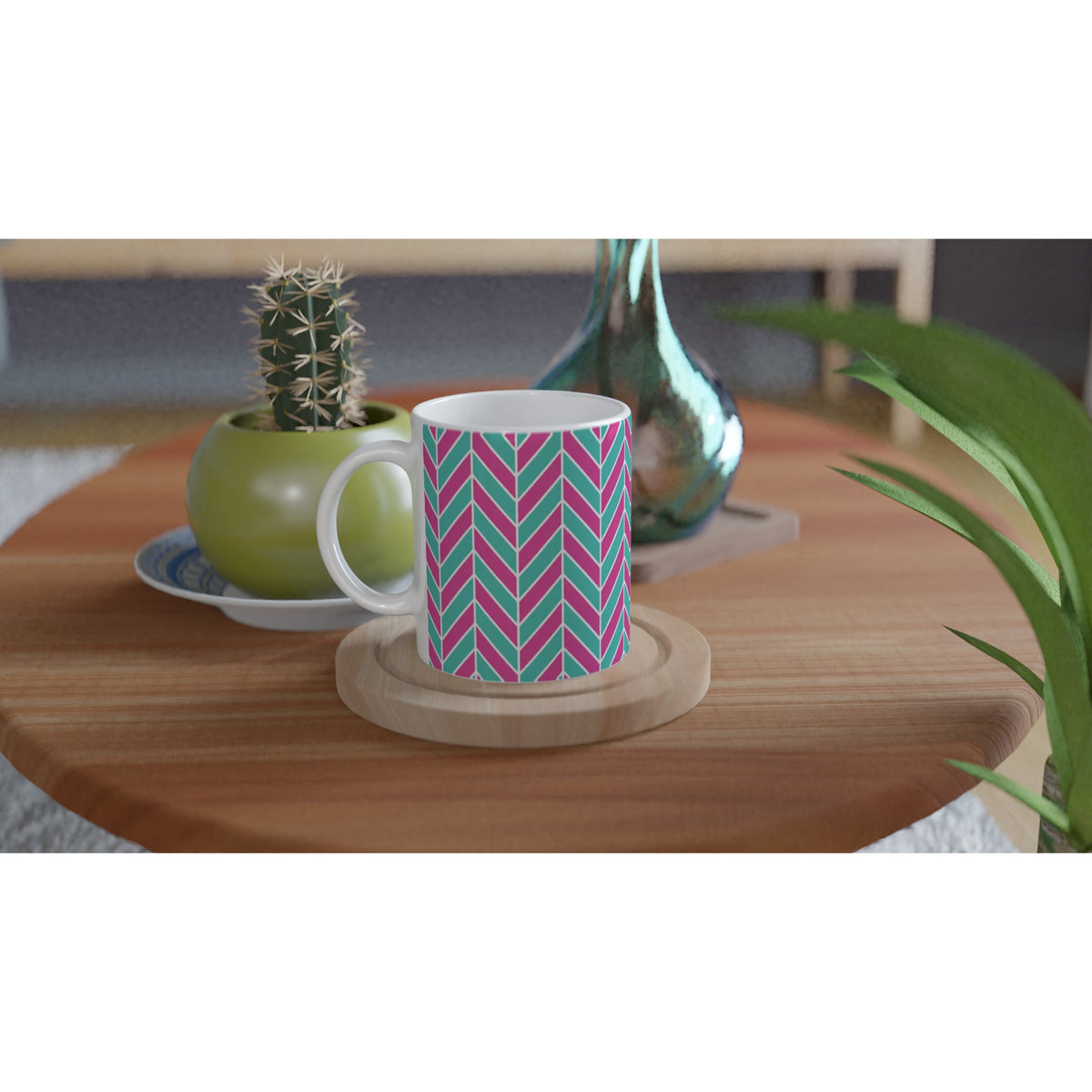Pink and aqua herringbone ceramic mug with retro geometric pattern on wooden coaster beside small cactus.