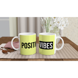 Two lime mugs with bold POSITIVE VIBES text on a wooden table; floral bouquet in the background.