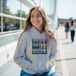 Woman wearing grey retro cassette tape graphic hoodie featuring six vintage 90s style music tapes in a colorful grid pattern.