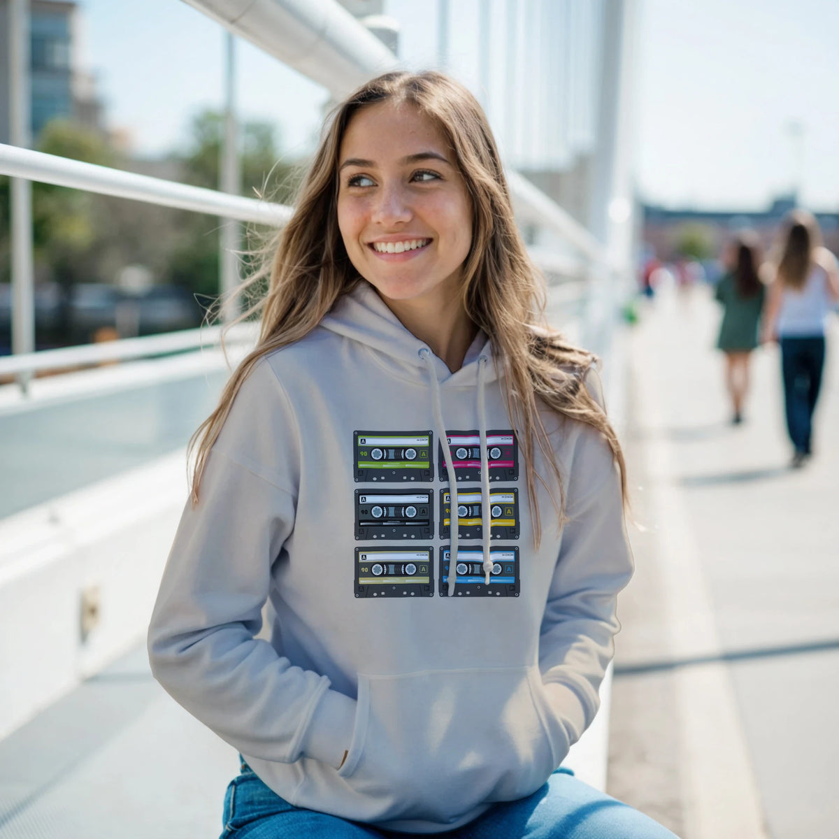 Woman wearing grey retro cassette tape graphic hoodie featuring six vintage 90s style music tapes in a colorful grid pattern.