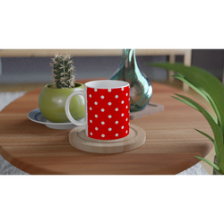 Red and white polka dot ceramic mug on a wooden coaster next to a small cactus and teal glass vase.