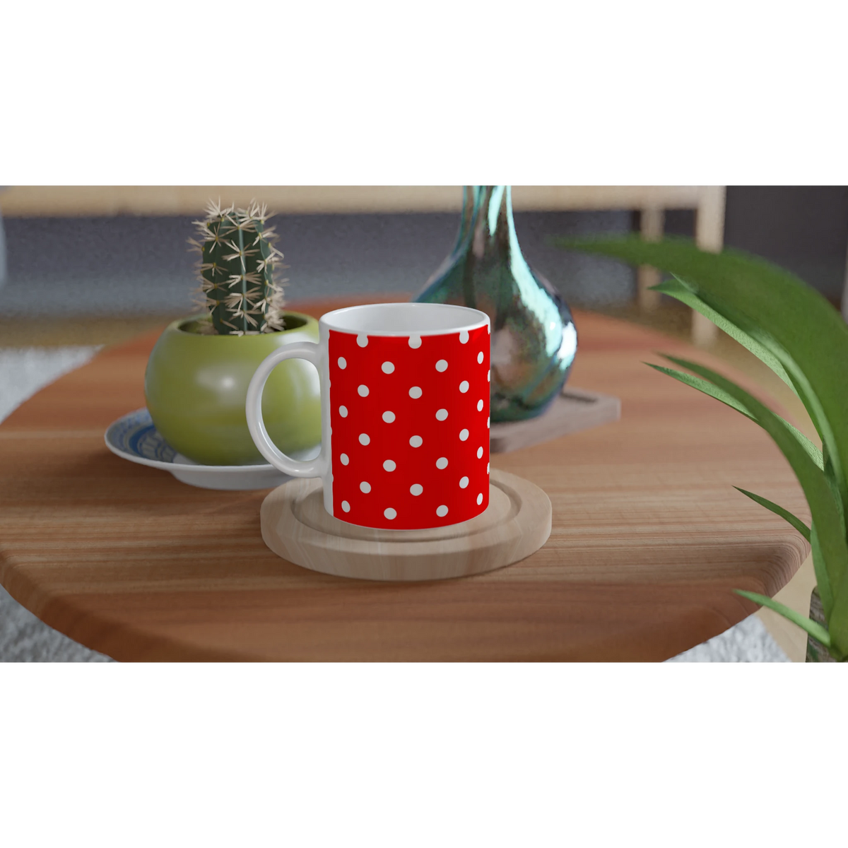 Red and white polka dot ceramic mug on a wooden coaster next to a small cactus and teal glass vase.